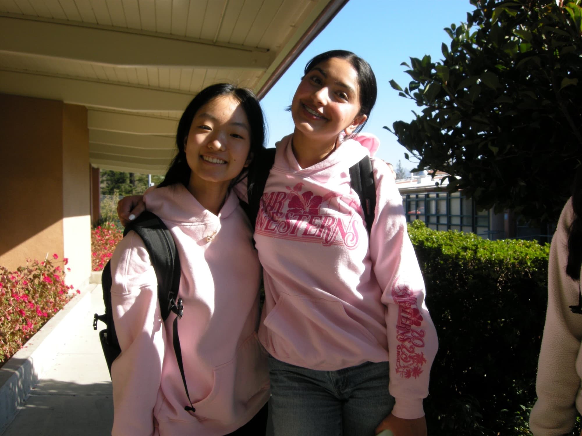 Two students in pink hoodies outside on campus, arms around each other.